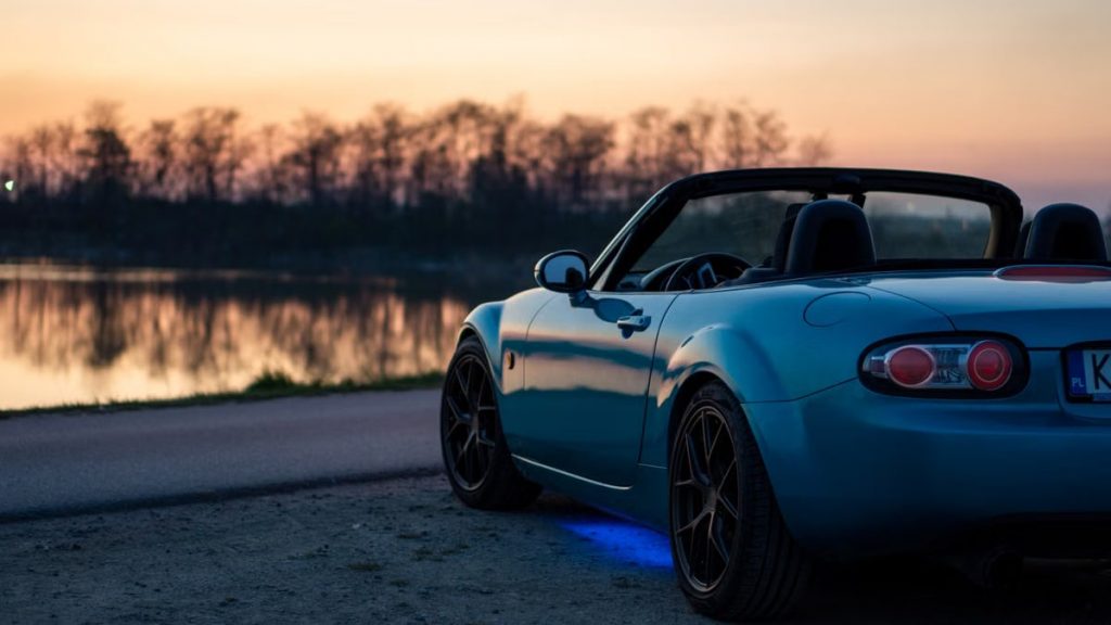 A sports car parked by a lake at sunset in Brzegi, Poland, offering a scenic view.