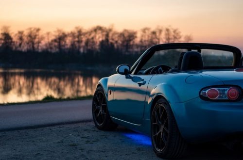A sports car parked by a lake at sunset in Brzegi, Poland, offering a scenic view.
