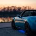 A sports car parked by a lake at sunset in Brzegi, Poland, offering a scenic view.